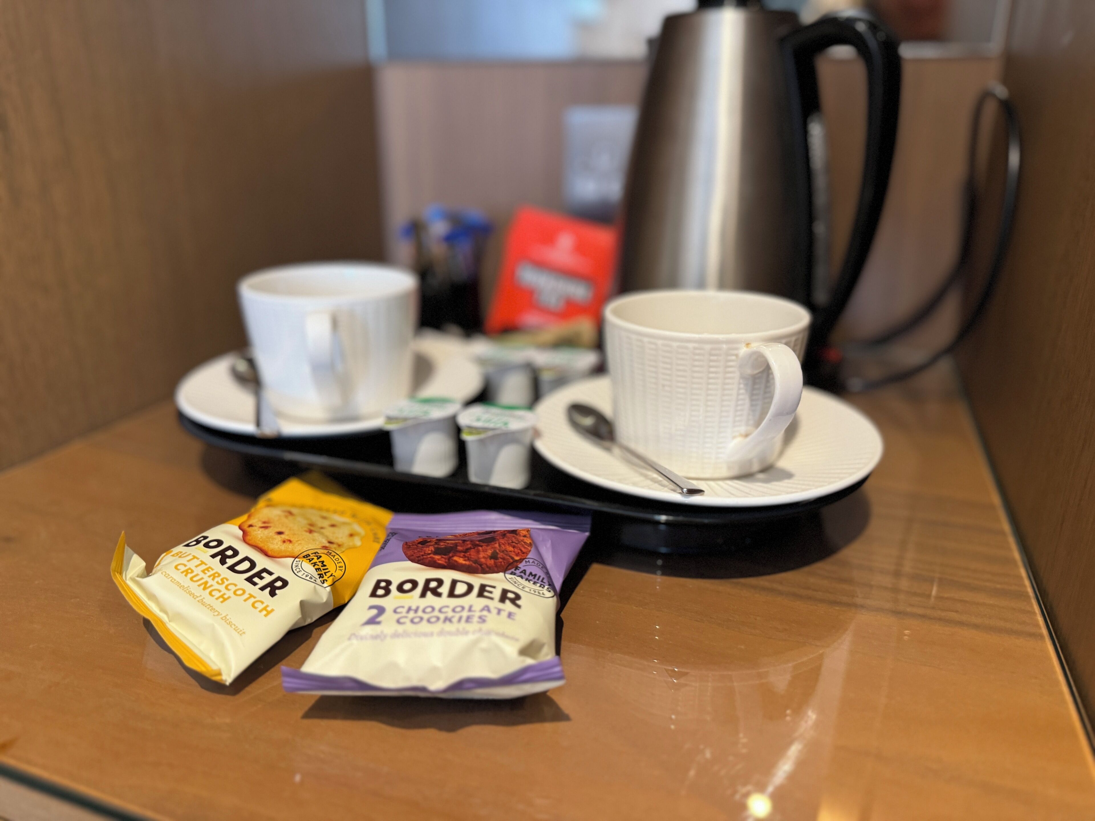 Bandeja de desayuno con dos tazas, una cuchara, una tetera y dos paquetes de galletas Border.