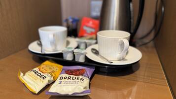 A breakfast tray with two cups, a spoon, a kettle, and two packets of Border chocolate cookies.