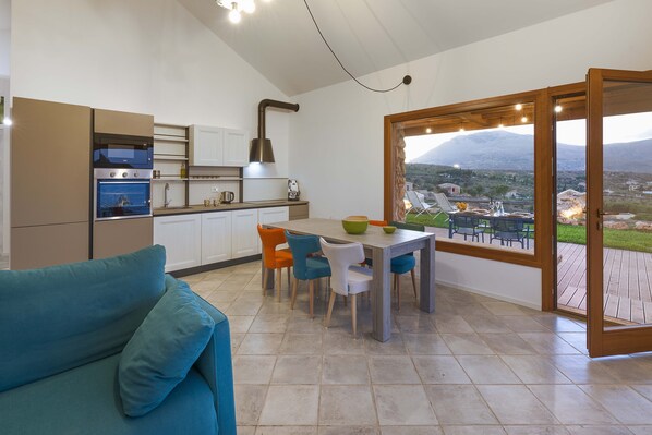 Une cuisine moderne dotée d’appareils électroménagers intégrés, un coin repas avec une table et des chaises, et une grande porte-fenêtre coulissante donnant sur un patio extérieur avec vue sur les montagnes.