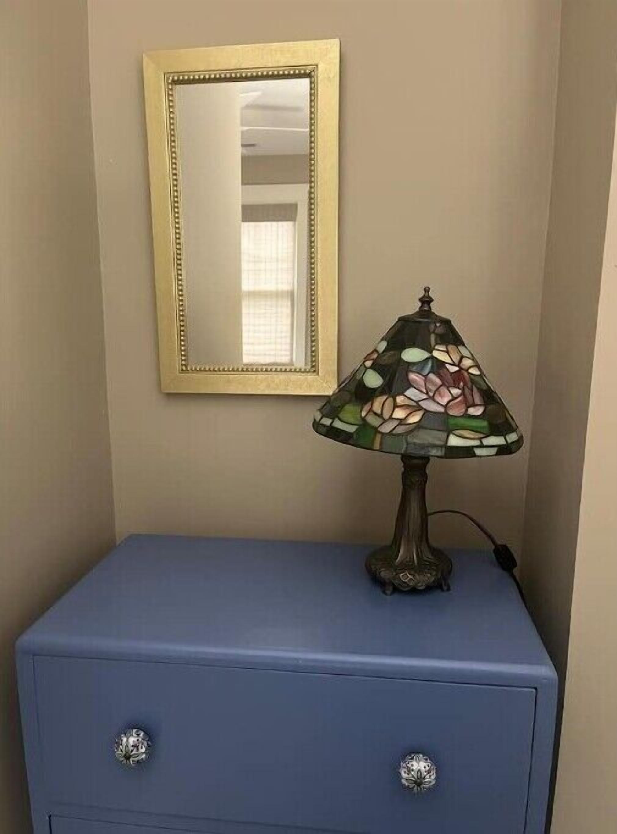 Quarto com cômoda azul, espelho e luminária de vitral.