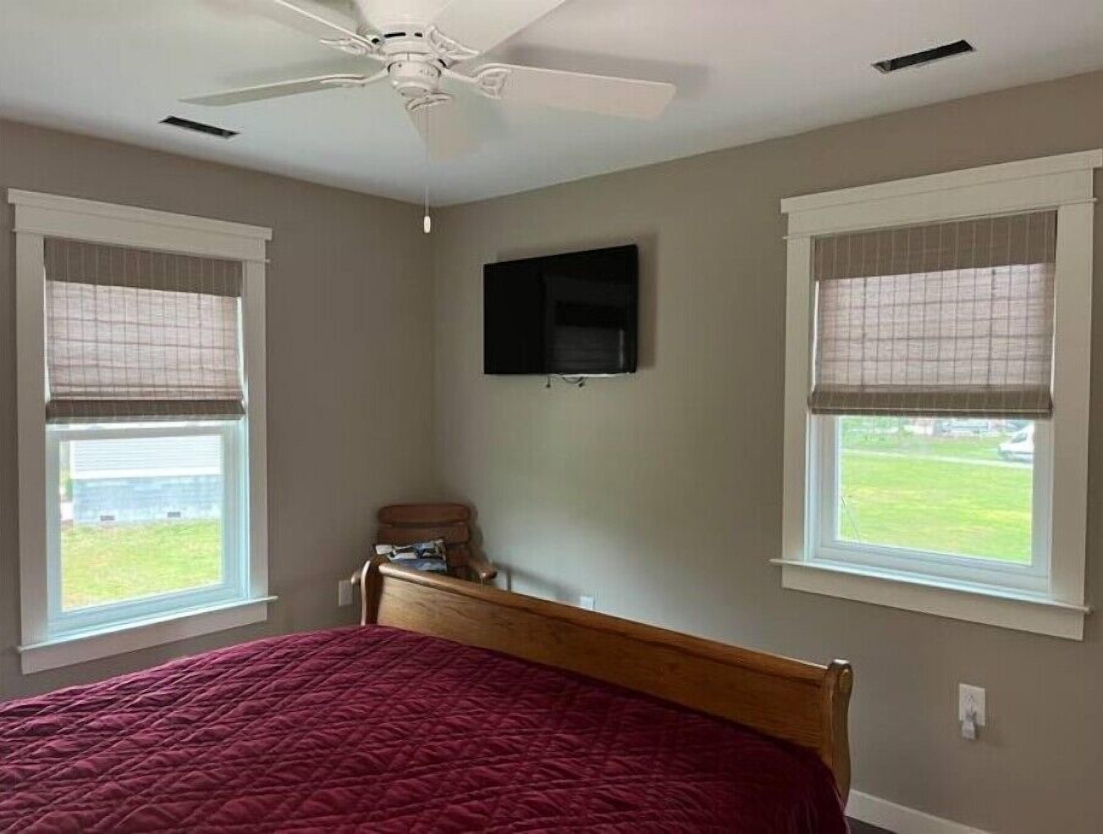 A bedroom with a bed, a ceiling fan, and two windows with blinds.
