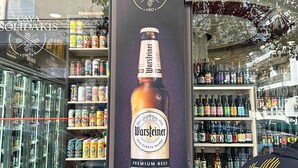 A storefront with a large advertisement for Warsteiner beer, shelves stocked with various beverages, and a person wearing a shirt with "URBAN LEGION" visible. - Beautiful studio close to the archaeological museum (Athina)