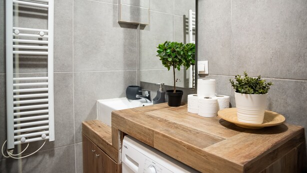 A modern bathroom with a wooden vanity, a white toilet, a towel rack, and a potted plant. - Beautiful studio close to the archaeological museum (Athina)