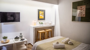 A hotel room with a bed, a desk with a lamp, a TV, and artwork on the walls. - Beautiful studio close to the archaeological museum (Athina)