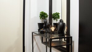 A corner of a room with a black metal console table against a white wall, a large mirror, and a door. - Beautiful studio close to the archaeological museum (Athina)