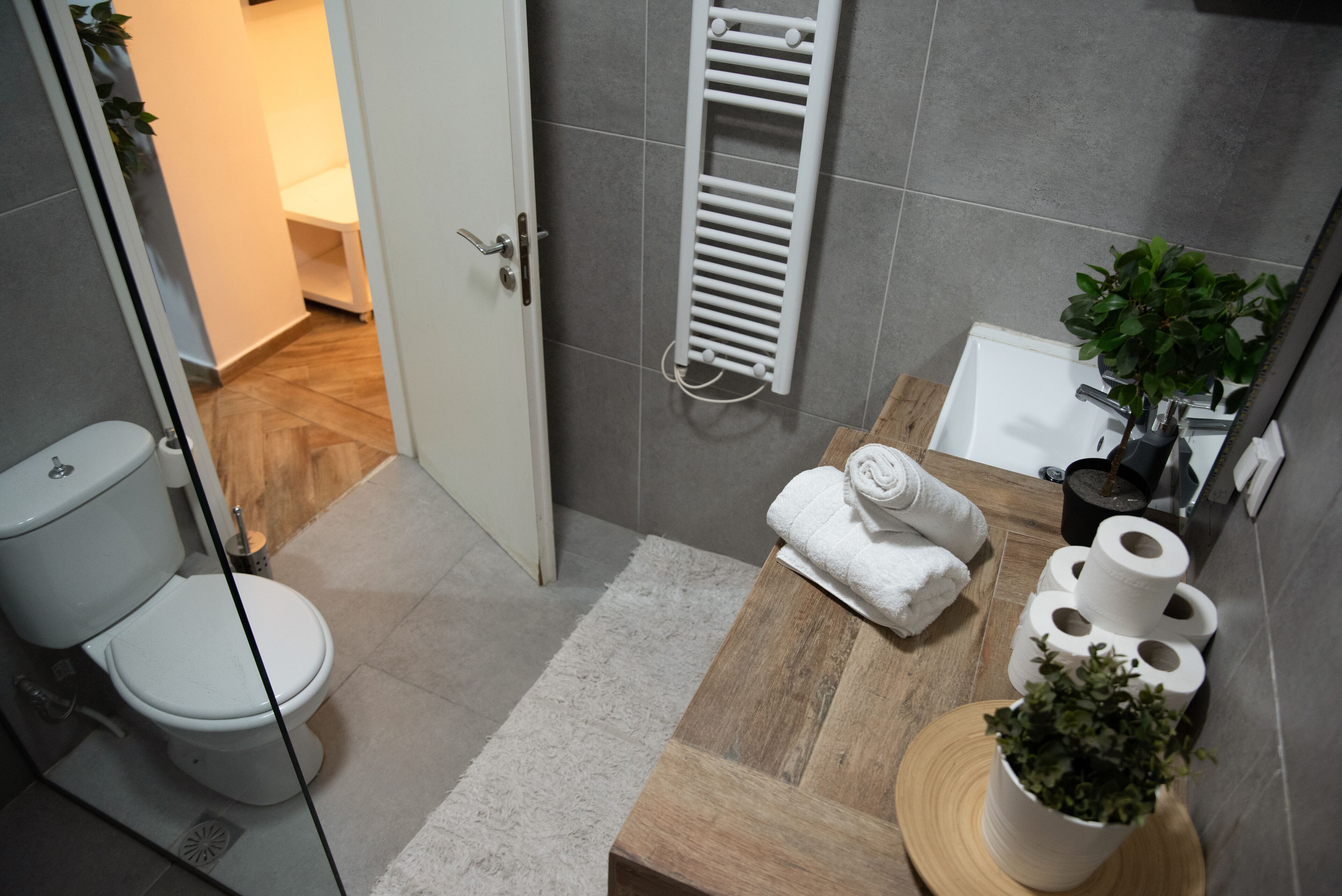 A modern bathroom with a toilet, a towel rack, a wooden vanity, and a potted plant.