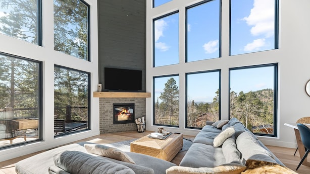 A spacious living room with a fireplace, large windows, and a view of trees.