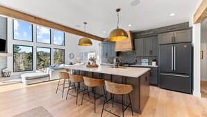 A modern kitchen with a central island, bar stools, and a large refrigerator.