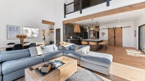 A modern living room with a sectional sofa, a wooden coffee table, and a dining area with a kitchen in the background.