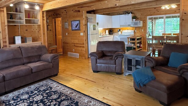 Een gezellig interieur van een chalet met houten wanden en vloeren, een woonkamer met twee banken, een eethoek en een keuken met witte kasten en een koelkast.