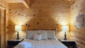 Een slaapkamer in een houten chalet met een bed, twee bedlampen en een schilderij aan de muur.