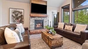 Un salon moderne avec une cheminée en pierre, des canapés en cuir et une grande fenêtre donnant sur la forêt.