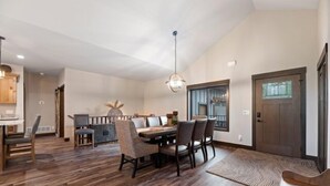 Un vaste espace dédié à la salle à manger, avec une table et des chaises en bois, un luminaire suspendu et une vue sur l’extérieur par une fenêtre.