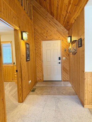 A wooden hallway with a white door, two wall-mounted light fixtures, and a framed picture on the left wall.