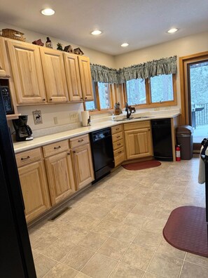 A kitchen with wooden cabinets, a dishwasher, a coffee maker, and a window with a checkered valance.