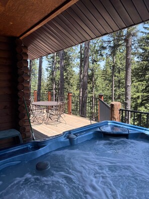 Un jacuzzi con cubierta de madera y vista a altos pinos.