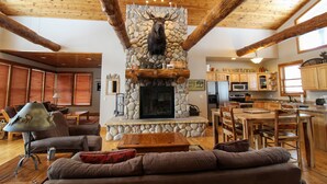 A rustic interior with a stone fireplace, wooden beams, a cozy seating area, and a kitchen with wooden cabinets. - Moose Trail Lodge- Terry Peak with Hot Tub (Lead)