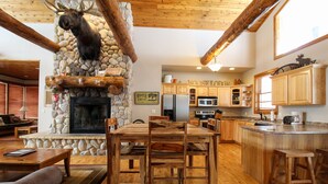 A rustic interior with a stone fireplace, wooden furniture, and a kitchen area. - Moose Trail Lodge- Terry Peak with Hot Tub (Lead)
