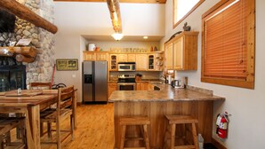A cozy kitchen with wooden cabinets, a stone fireplace, and a stone wall. - Moose Trail Lodge- Terry Peak with Hot Tub (Lead)