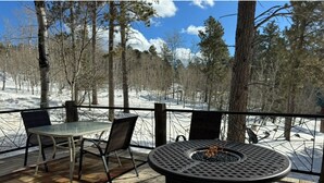 A deck with a round table and chairs, a fire pit, and a view of a snowy forest. - Moose Trail Lodge- Terry Peak with Hot Tub (Lead)