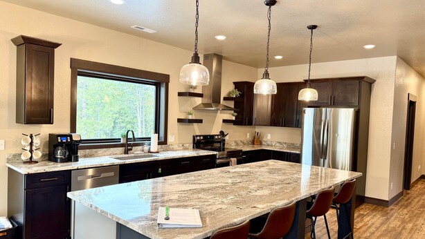 A modern kitchen with a large island, dark wood cabinets, stainless steel appliances, and pendant lighting. - Moonlit Summit with hot tub, lots of great parking and views (Lead)