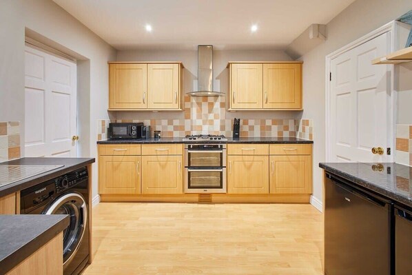 Une cuisine moderne avec des meubles de rangement en bois, un four encastré, un four à micro-ondes et un lave-vaisselle.