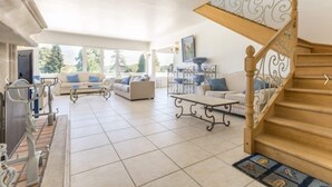 Amplia sala de estar con escalera de madera, varios sofás y una mesa de comedor.