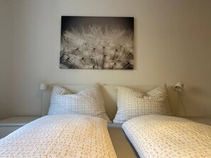 Un dormitorio con dos camas, cabeceras, una lámpara de pared y un cuadro sobre las camas.