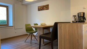 Une cuisine moderne avec une table en bois, des chaises vertes, une machine à café et un tableau accroché au mur.