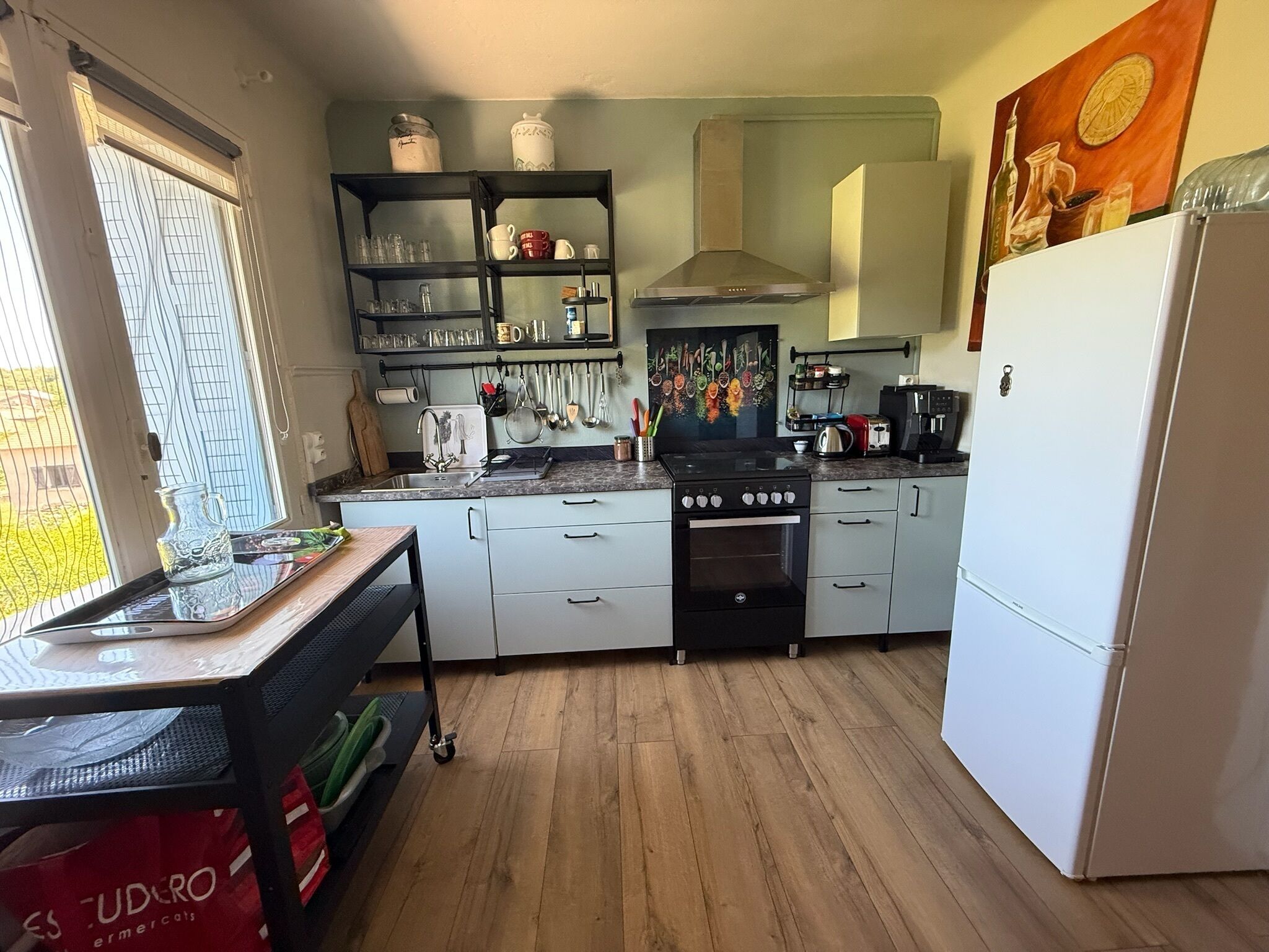 Una cucina con fornello, forno, frigorifero ed scaffali pieni di utensili da cucina.