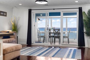 A living room with a sofa, a coffee table, and a view of the ocean through large glass doors. - Million Dollar View Bayshore Beach House (Traverse City)
