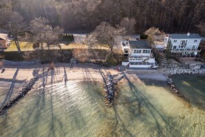 A residential area with a house near a body of water, surrounded by trees and a stone wall. - Million Dollar View Bayshore Beach House (Traverse City)