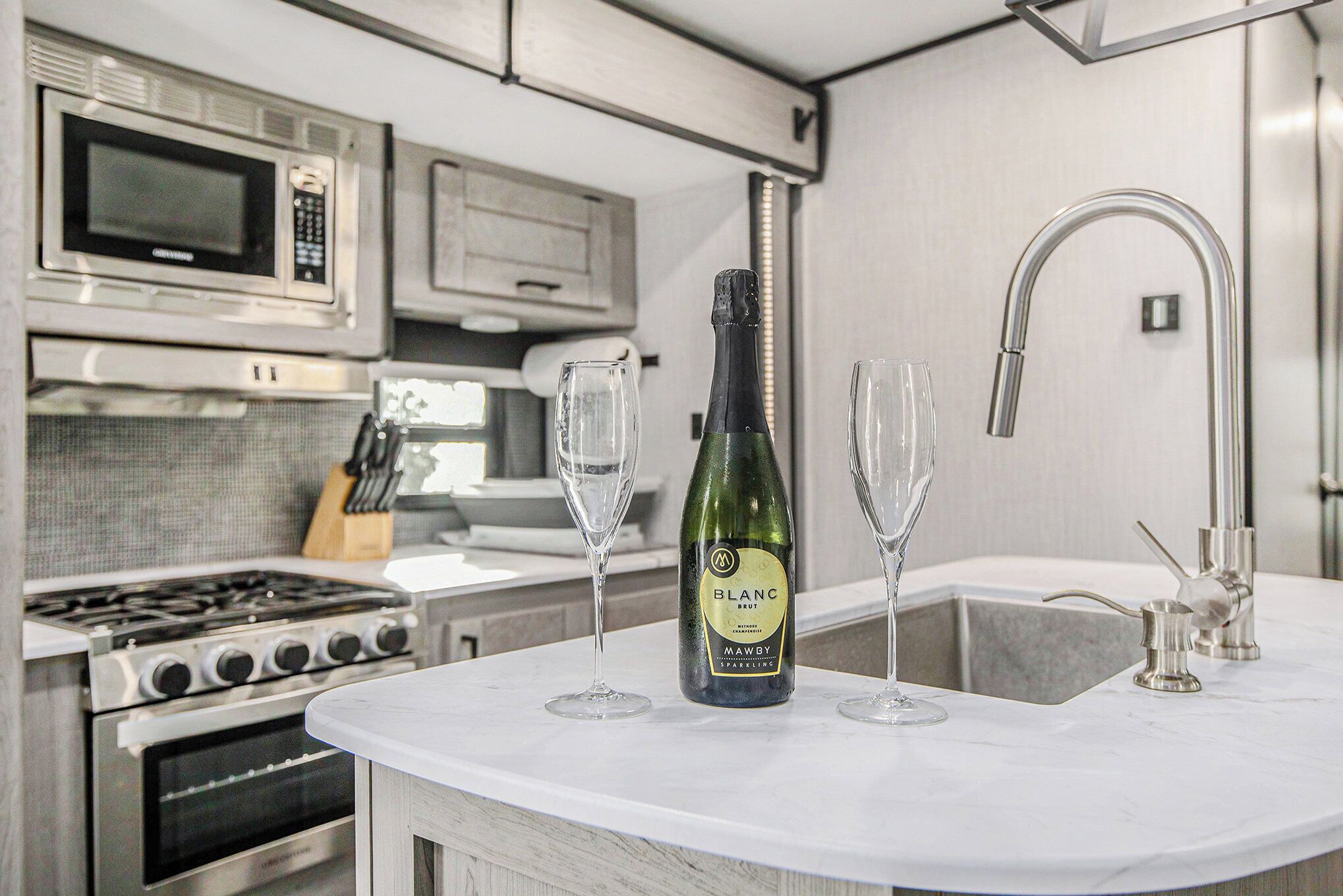 Una cocina con microondas, estufa, botella de vino y vasos.