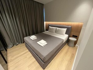 A modern hotel room with a large bed, grey bedding, and a wooden floor.