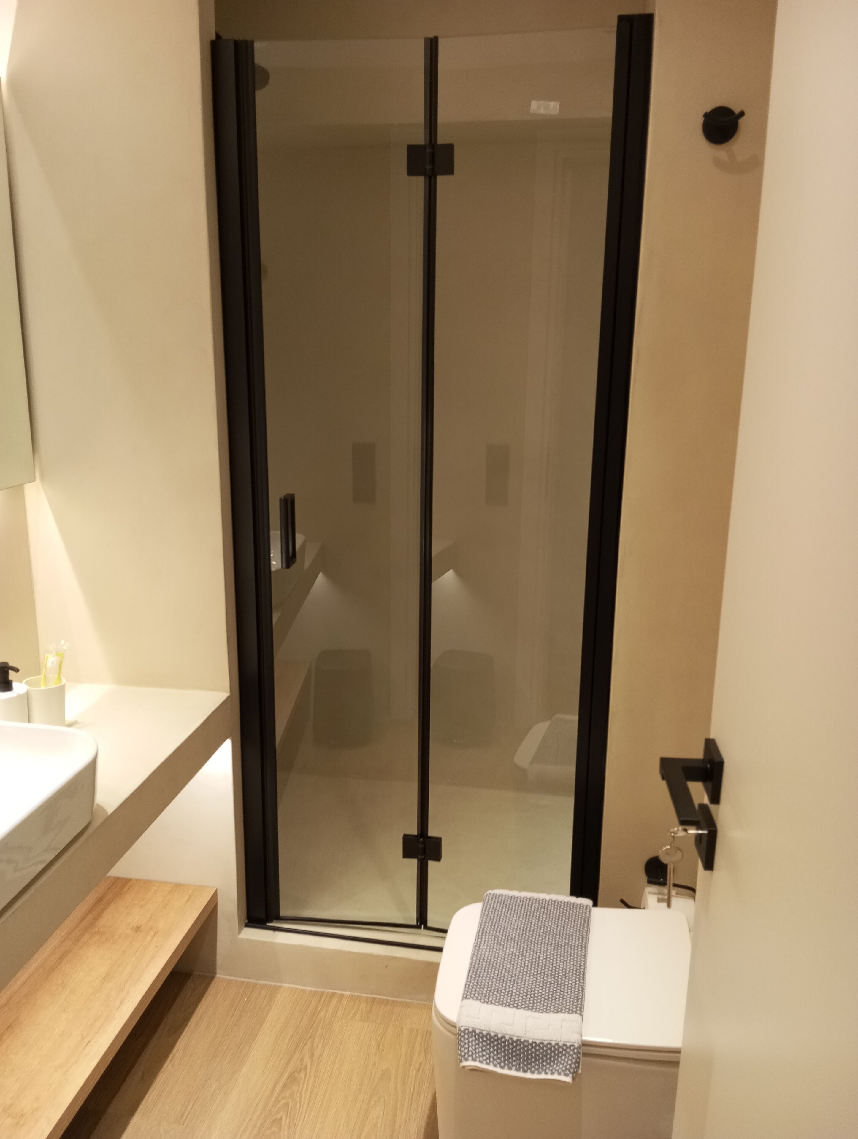 A modern bathroom with a glass shower enclosure, a wooden vanity, and a toilet with a towel.