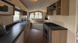 A compact kitchen with a microwave, stove, and sink, leading to a seating area with a view. - Prime Lakeside Caravan at Haven Golden Sands (Mablethorpe)