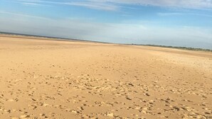 A wide sandy beach with footprints, a clear sky, and distant vegetation. - Prime Lakeside Caravan at Haven Golden Sands (Mablethorpe)
