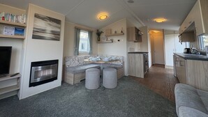 A compact living space with a kitchenette, a dining area with a table and chairs, a sofa, and a fireplace. - Prime Lakeside Caravan at Haven Golden Sands (Mablethorpe)
