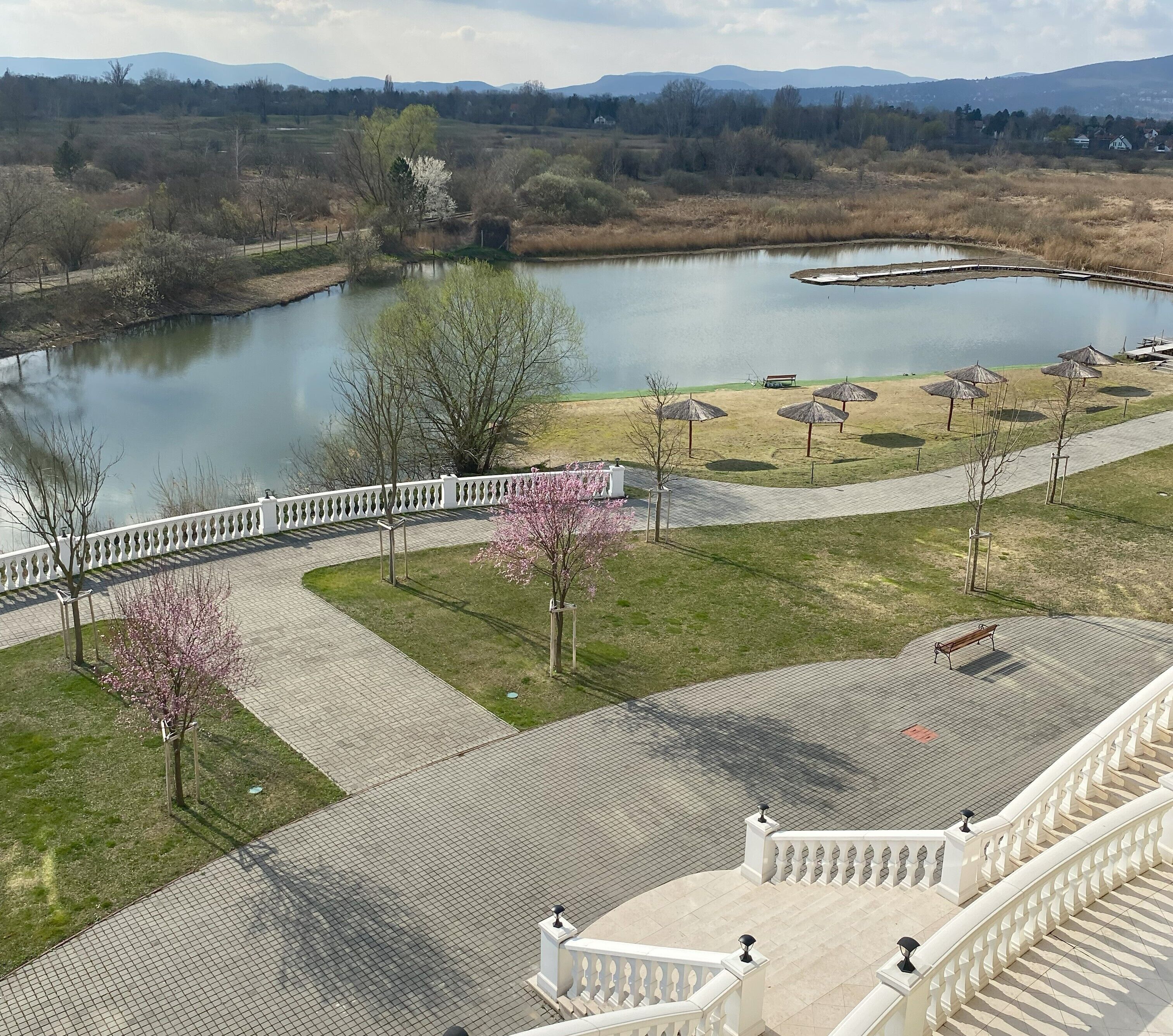 A park with a pond, walking paths, benches, and a white fence.
