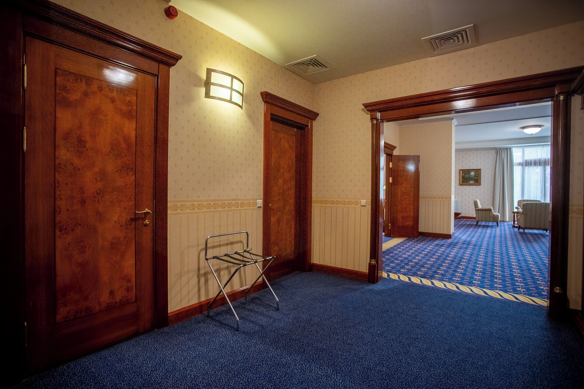 Ein Hotelkorridor mit Holztüren, einem Metallgestell und einem gemusterten Teppich.