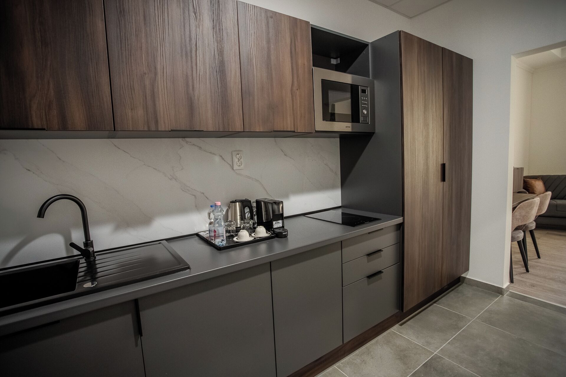 Una cocina moderna con armarios de madera oscura, un microondas empotrado, un lavamanos de acero inoxidable y un salpicadero de mármol.