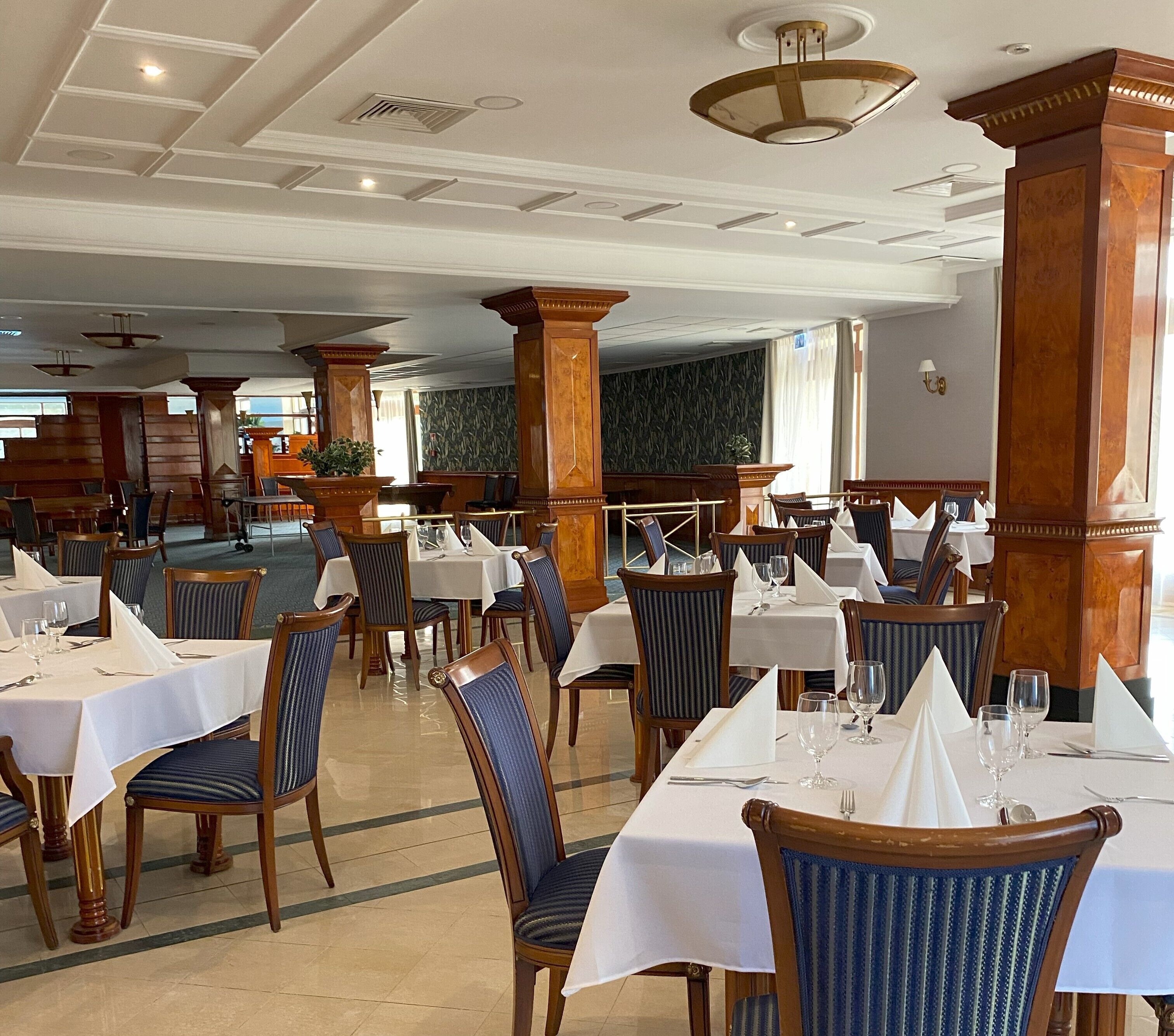 A spacious dining area with multiple tables and chairs, large wooden pillars, and a high ceiling with recessed lighting.