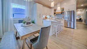 Une cuisine moderne avec un plancher en bois, des meubles blancs, un îlot central doté de tabourets et des appareils électroménagers en acier inoxydable.