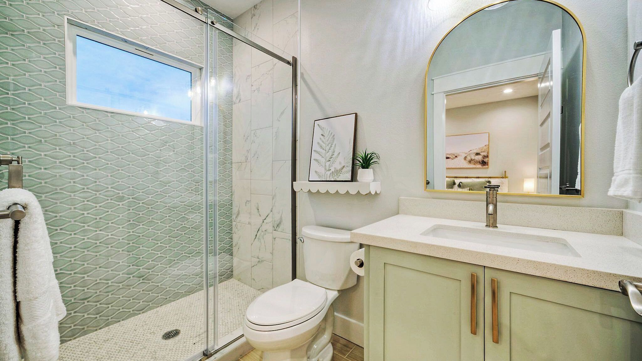 Un baño con cabina de ducha de vidrio, inodoro, lavabo con espejo y toallero.