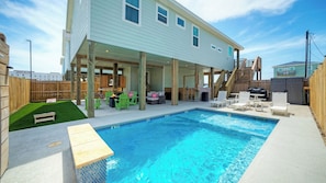 A swimming pool with a covered patio area, wooden deck, and outdoor seating. - Swinging Easy by Avantstay Private Pool, Firepit, Balcony (Port Aransas)
