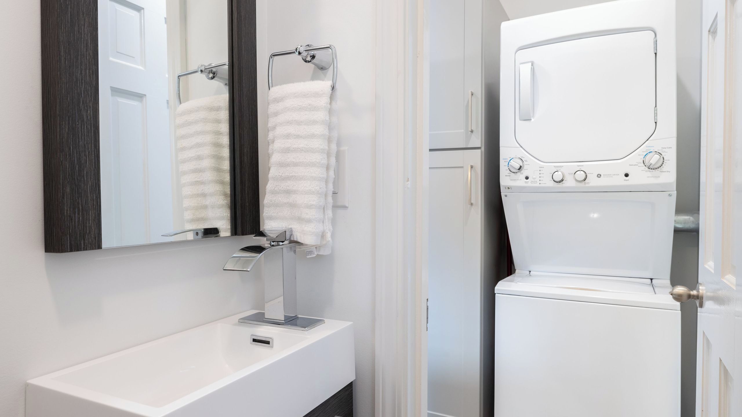 Une salle de bain moderne avec un lavabo blanc, deux porte-serviettes, un miroir et un lave-linge à chargement frontal.