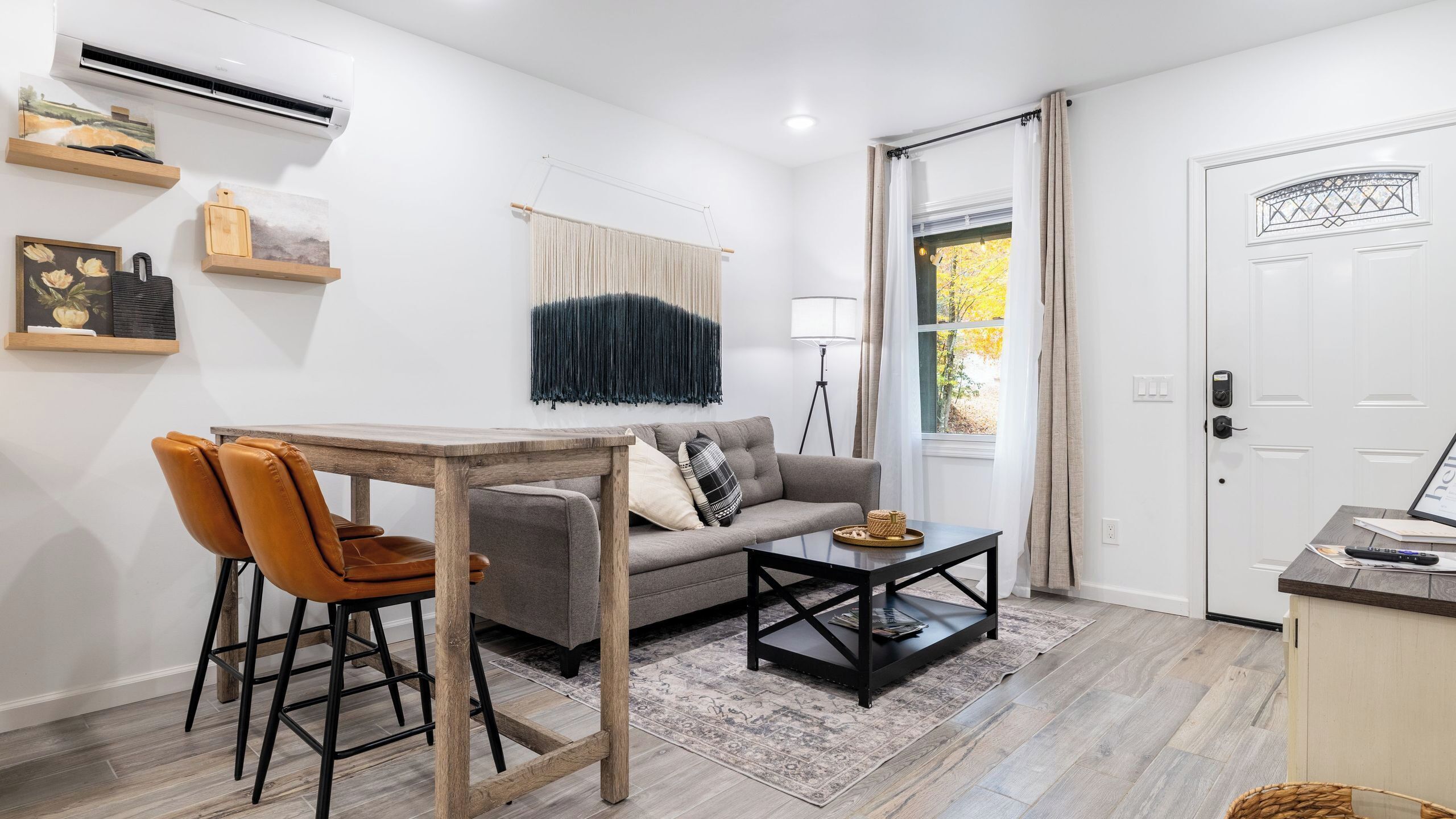A modern living room with a sofa, coffee table, and chairs, a dining table, a lamp, and a door with a window.
