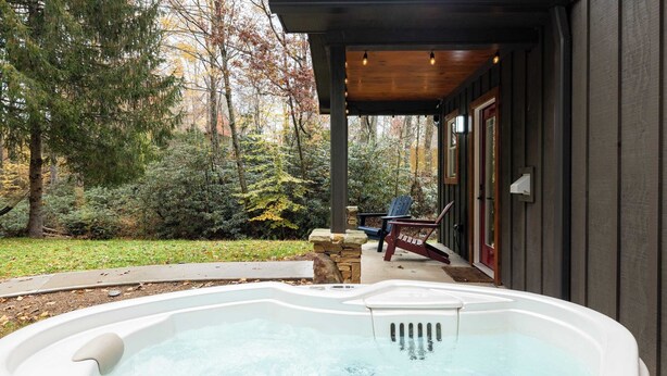 Un bain à remous situé dans un espace extérieur abrité, doté d’une terrasse en bois et offrant une vue sur une forêt.