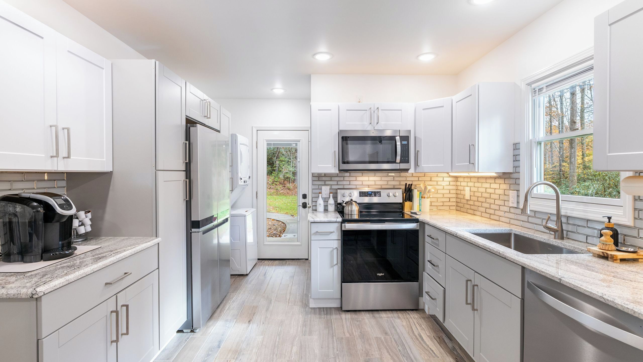 A modern kitchen with white cabinets, stainless steel appliances, and a brick backsplash.