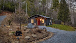 Une cabane avec une porte rouge, entourée d’une forêt, et un panneau d’avertissement représentant un ours au premier plan.